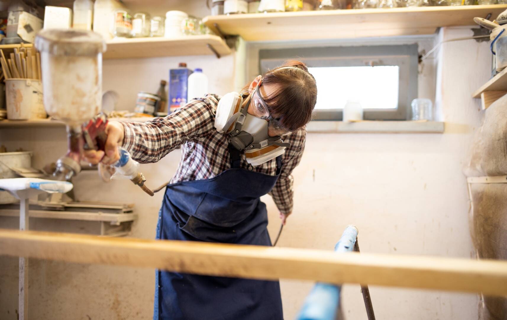 Young woman craftswoman applying varnish on wooden elements in woodshop